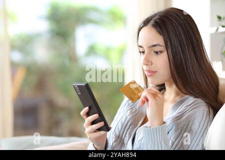 Donna seria che acquista online con carta di credito e cellulare seduto su un divano a casa Foto Stock