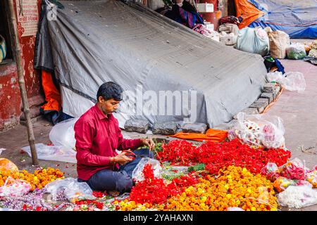 Un venditore locale detiene ghirlande di ibisco che sta facendo nel mercato dei fiori di Howrah a Strand Bank Road, Kolkata (Calcutta), Bengala Occidentale, India Foto Stock