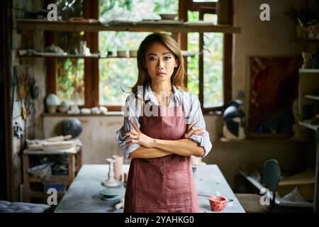 Artista donna di successo che posa in un laboratorio creativo con la sua opera d'arte sullo sfondo. Hobby, concetto di persone creative Foto Stock