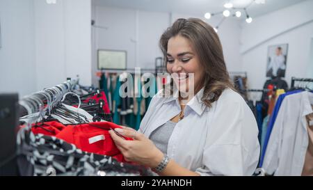 Una donna grassa guarda con orrore al prezzo di un abito in un negozio Plus size. Foto Stock