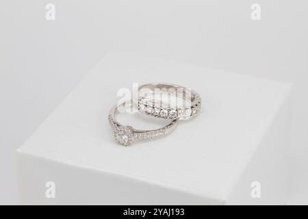 due anelli di diamante dorati posizionati su una superficie bianca, caratterizzati da design intricati e diamanti scintillanti. Foto Stock