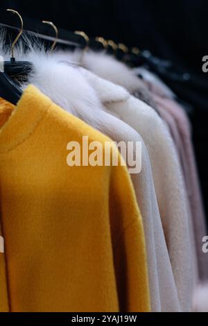 Cappotti in pelliccia gialla e bianca per donne appese in fila su grucce in una boutique di abbigliamento di lusso invernale Foto Stock