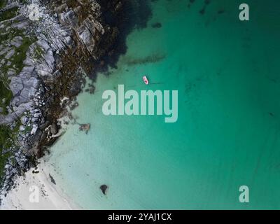 Vista aerea della barca rossa che galleggia nelle acque cristalline turchesi vicino alla costa rocciosa Foto Stock