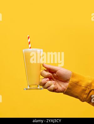 Indossa un caldo maglione a maglia che regge un bicchiere di idromele caldo con paglia rosso-bianca su uno sfondo giallo caldo. Foto Stock