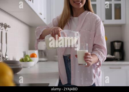 Giovane donna versando latte da gallone bottiglia in vetro vicino al piano di lavoro leggero in cucina, primo piano Foto Stock