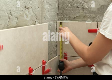 Donna che piastrella le pareti del bagno, utilizzando un metro a nastro per misurare la lunghezza. Processo di installazione delle piastrelle nel bagno passo dopo passo. Miglioramento fai da te Foto Stock