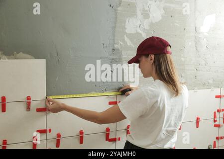 Donna che piastrella le pareti del bagno, utilizzando un metro a nastro per misurare la lunghezza. Processo di installazione delle piastrelle nel bagno passo dopo passo. Miglioramento fai da te Foto Stock