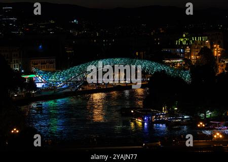 Scena notturna guardando verso il basso l'iconico ponte della pace illuminato e riflesso nel fiume kura a Tbilisi in georgia Foto Stock