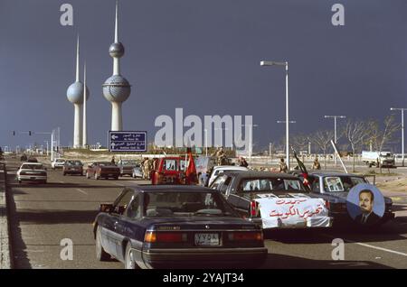 Prima guerra del Golfo: 8 marzo 1991 le persone celebrano la liberazione del Kuwait da parte delle forze della coalizione. A sud delle iconiche Torri d'acqua, le auto sulla Arabian Gulf Street di Kuwait City espongono poster e ritratti dell'emiro e del principe ereditario del Kuwait e del presidente siriano Hafez al-Assad. Foto Stock