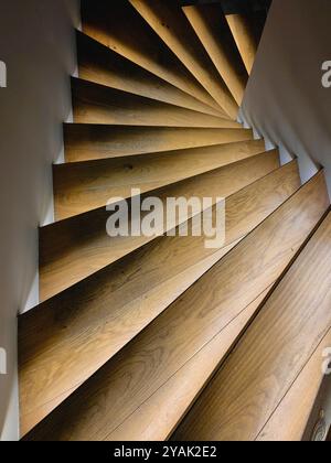 Scala curva in legno marrone chiaro con luci a LED. Infinito, concetto. Design moderno. Forma. Muro bianco, sfondo. Su o giù, dipende da te. Foto Stock