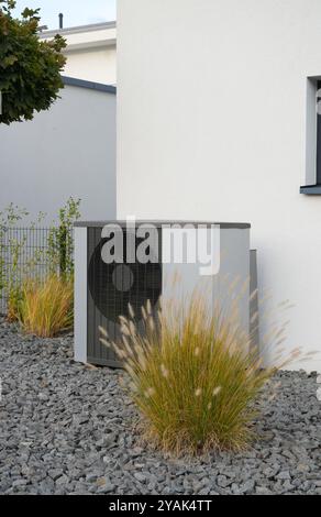 Pompa di riscaldamento di fronte a una nuova casa con giardino e alcune piante decorative Foto Stock