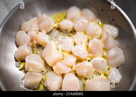 Capesante frittura di pesce sul piatto macro primo piano di un piattino in acciaio inossidabile, saltando olio d'oliva aglio fresco cucinando a fuoco nella cucina di casa Foto Stock