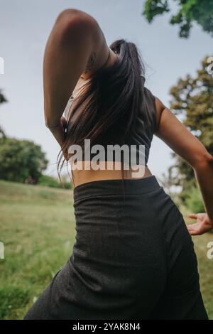 Donna che si diverte a ballare in un parco lussureggiante con un'espressione serena, sentendosi libera e connessa alla natura in una giornata di sole. Foto Stock