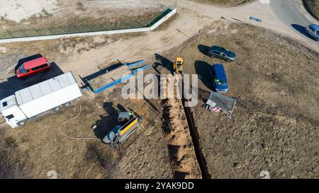 Vista aerea dei lavoratori edili che scavano una trincea in un campo durante il sole primaverile Foto Stock