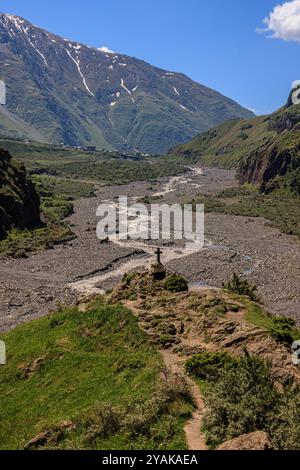 ammira la ripida gola di dariali in georgia, una croce di pietra che guarda in basso su uno stretto fiume tortuoso in una valle rocciosa Foto Stock