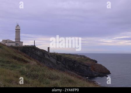 Il faro di Santander su scogliere rocciose che si affacciano su un oceano calmo sotto un cielo nuvoloso in Cantabria, Spagna. Foto Stock