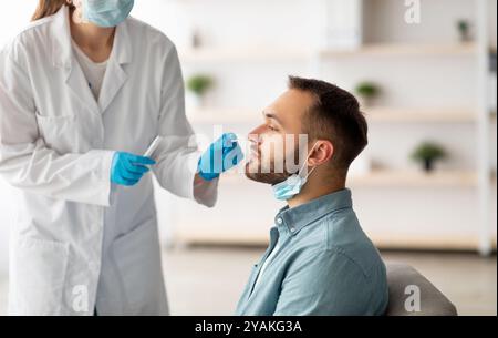 Procedura diagnostica Covid. Medico che fa test PCR nasale per l'uomo giovane caucasico, utilizzando bastoncino di tampone sterile a casa Foto Stock