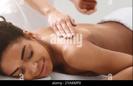 Massaggiatrice applicando scrub corpo sulla schiena ragazza nera Foto Stock