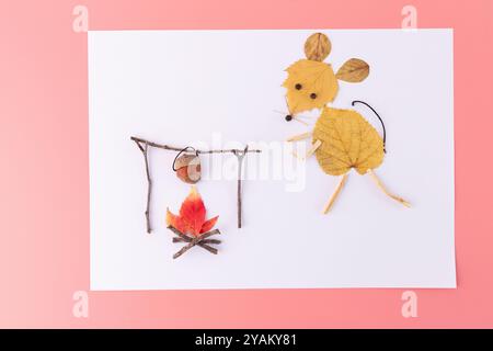 Topo fatto di foglie d'autunno gialle in piedi vicino a un falò, composizione piatta minimalista con spazio di copia. Campeggio autunnale e artigianato naturale, rosa Foto Stock