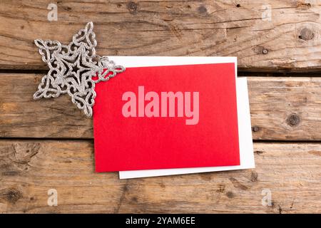 Un biglietto d'auguri natalizio poggia su una superficie di legno, con spazio per le copie. Lo spazio rosso vuoto della carta consente di personalizzare il messaggio o il design delle vacanze. Foto Stock