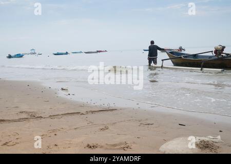 Un pescatore sta portando la sua barca sulla spiaggia Foto Stock