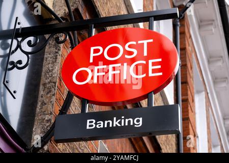 Un cartello con l'appeso dell'ufficio postale sul lato di un edificio lungo una strada principale locale a Saffron Walden, Essex, Regno Unito. Foto Stock