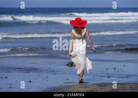 Una donna mozzafiato si crogiola nella beatitudine della spiaggia, vicino a un molo, sotto cieli azzurri, abbracciando la serenità di una giornata perfetta in riva al mare Foto Stock