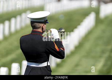 Un momento toccante si svolge mentre un Marine gioca a rubinetti, onorando un veterano caduto con un solenne saluto, segnando il loro internamento in un ceme militare nazionale Foto Stock