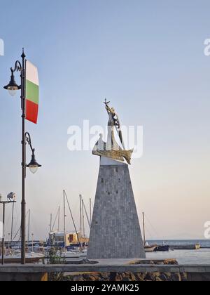 La statua di San Nicola patrono dei marinai nella città vecchia di Nessebar, Bulgaria. Calmo tramonto al porto con barche attraccate in acque calme, una mostra Foto Stock