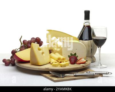 Composizione di formaggio, uva, bottiglie e bicchieri di vino e fragole su un vassoio rotondo di legno su una tovaglia bianca, isolato su uno sfondo bianco Foto Stock