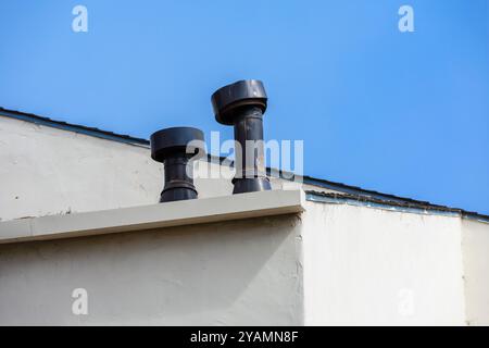 Due tubi di ventilazione metallici si innalzano dal tetto di un edificio, con un tubo disallineato. Foto Stock