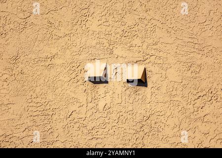 Due bocchette di scarico dell'aria sporgono da una parete in stucco beige testurizzato. Foto Stock