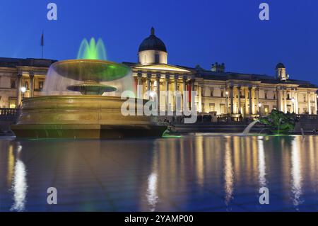 Trafalgar Square in serata, la Galleria Nazionale. In primo piano, fontana illuminata e piscina, che riflettono il cielo e le luci. Londra, Regno Unito Foto Stock