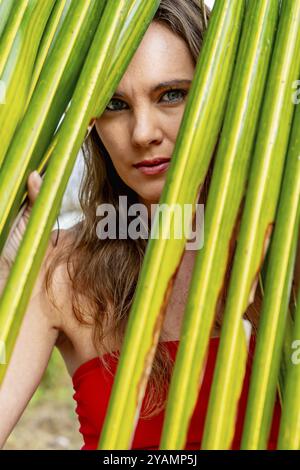 La splendida bruna, splendente in un vivace abito rosso, abbellisce le coste caraibiche con eleganza, incarnando la bellezza nel paradiso tropicale Foto Stock