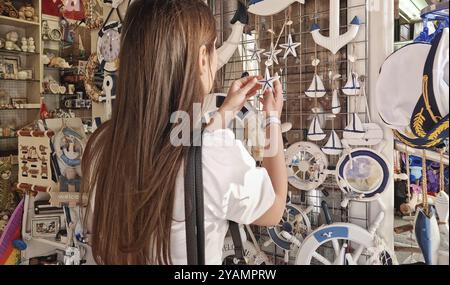 Giovane cliente donna all'interno di un negozio di souvenir marini, scegliendo tra una varietà di oggetti decorativi a tema nautico sugli scaffali del mercato Foto Stock