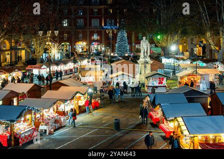 Persone che camminano tra i chioschi sulla piazza della città illuminata e decorata per le vacanze di Natale ad Asti, Italia. Foto Stock