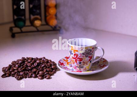 Una tazza di caffè caldo emette vapore, circondato da ricchi chicchi di caffè e da un moderno portacialde, perfetto per gli amanti del caffè Foto Stock