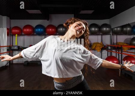 Una donna gioiosa balla liberamente in una sala fitness piena di palline colorate, che irradiano positività ed energia intorno a mezzogiorno Foto Stock