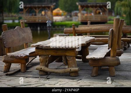 Panca rustica in legno e tavolo adagiati sul patio sul lago in un parco tranquillo in una giornata tranquilla Foto Stock