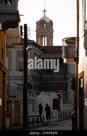 Nicosia, Cipro - 3 dicembre 2022: Due uomini che camminano lungo una stretta strada con la torre della chiesa Faneromeni sullo sfondo Foto Stock
