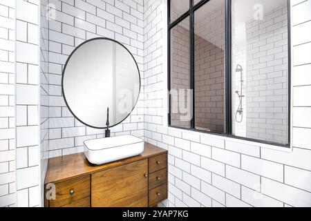 Bagno dal design moderno ed estetico con specchio circolare e elegante lavandino in legno Foto Stock