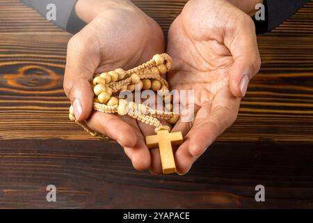 Uomo che mostra un rosario in mano su uno sfondo di legno. Simbolo della fede e del culto in Dio. La gente il cristianesimo la preghiera in chiesa. Servi religiosi Foto Stock