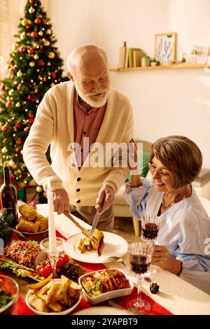 Una coppia senior si gode una cena natalizia, circondata da un albero splendidamente decorato. Foto Stock