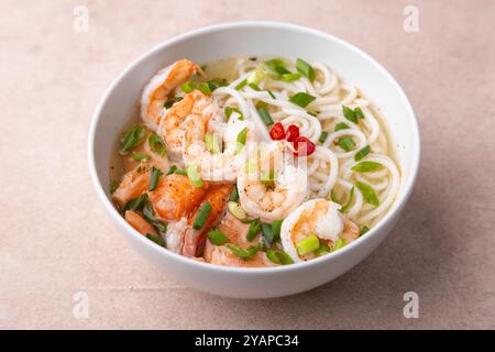 Piatto asiatico con brodo, tagliatelle, gamberi tigre, pesce e cipolle verdi. Zuppa tradizionale asiatica in un piatto profondo bianco. Messa a fuoco selettiva, primo piano. Foto Stock