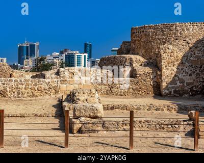 Le rovine della fortezza del Bahrein Qal'at al-Bahrain e lo skyline di Manama in Bahrein Foto Stock