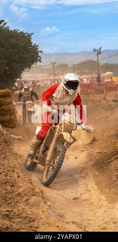 Il pilota di Motocross che fugge dal suo inseguitore prendendo una curva in piedi sulla sua moto, girandola lateralmente su una pista di sterrato all'aperto, generando un sacco di cose Foto Stock