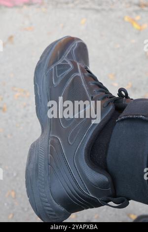 Primo piano di una scarpa sportiva nera su un fondo grigio con foglie gialle sparse. Foto Stock