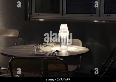 Un bicchiere d'acqua si trova su un tavolo accanto a una lampada. La lampada proietta un'ombra sul tavolo, creando un senso di profondità e dimensione. La scena è semplice Foto Stock