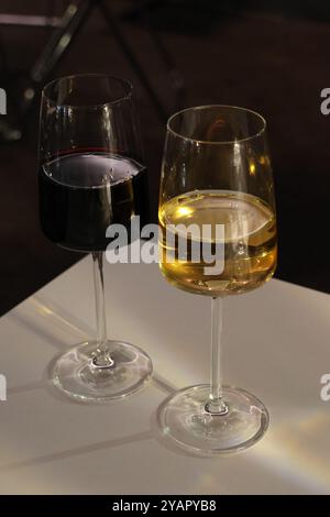 Due bicchieri da vino, uno rosso e uno bianco, seduti su un tavolo. Il vino rosso è quasi scomparso, mentre il vino bianco è quasi pieno. Gli occhiali sono i prossimi Foto Stock