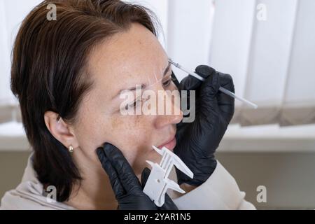 Evidenziando la precisione della mappatura delle sopracciglia: La preparazione di una donna per il trucco permanente. Foto Stock